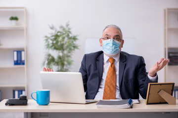 Old male employee working in the office during pandemic