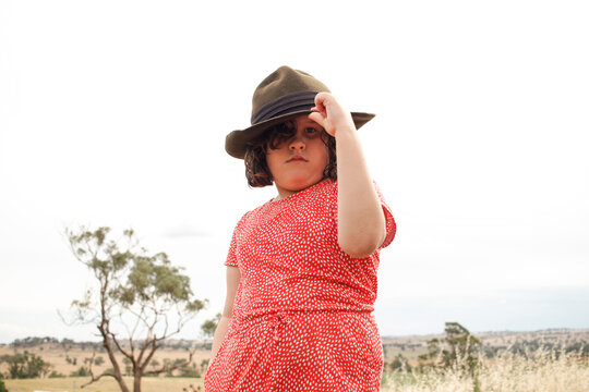 Mid-shot of young girl in grassy field wearing a red dress and blue bucket hat