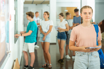 Fototapeta na wymiar Teenage girl standing in school's hallway. Group of young students standing in line in background.