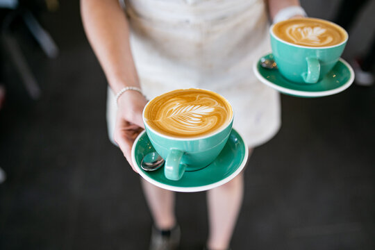 Top view shot of 2 cups of coffee with an art in a green cup being carried by a woman