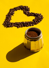 Vertical close-up of mocha coffee pot with ground coffee and coffee beans in the back in heart shape in the background