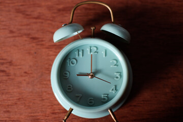 Classic turquoise alarm clock showing 9 oclock lying on wooden background