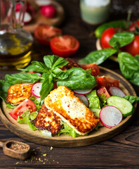Vegetable salad with fried cheese. Salad of fresh tomatoes, radishes, cucumbers, basil. Olive oil dressing. Lunch of fresh vegetables with halloumi Greek cuisine. Food styling of salad. Green food. 