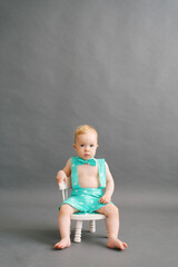 a one-year-old boy is sitting on a white children's chair on a gray background. Copy Space