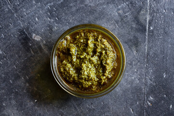 Pesto sauce in a glass bowl. Top view. Dark background.