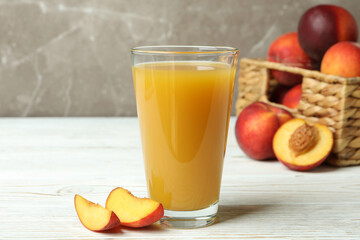 Glass of peach juice and peach fruits on white wooden table