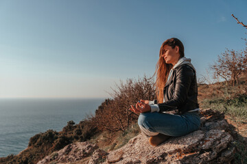 Naklejka na ściany i meble A young tourist Woman enjoying sunset over sea mountain landscape while sitting outdoor. Women's yoga fitness routine. Healthy lifestyle, harmony and meditation