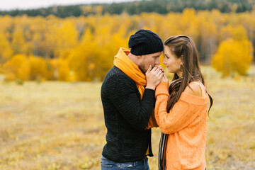 A guy warms the palms of his beloved girl against the background of the autumn landscape. Fall trip at the weekend