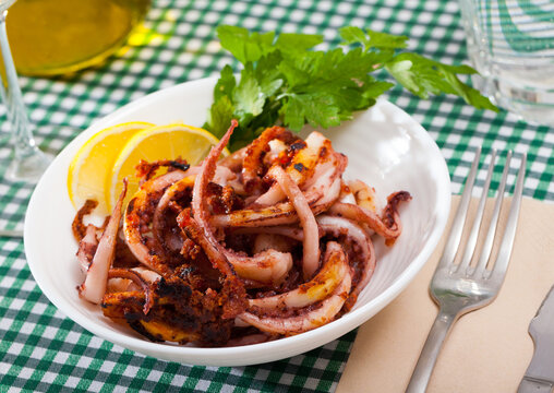 Delicious cooked squid or octopus tentacles with lemon and parsley on a plate. High quality photo
