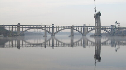Lustrzane odbicie budowy mostu przez rzekę Dniepr w Zaporożu, Ukraina - obrazy, fototapety, plakaty