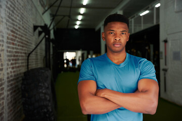African American male standing with crossed arms in the gym. Male personal trainer looking intensely at the camera. High quality photo