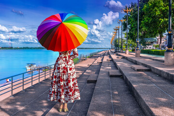 Thai woman holding a rainbow umbrella stands on the banks of the Mekong River in Nakhon Phanom...
