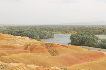 Desert landscape in Xinjiang, China, dry and colorful rocks, a river runs along and divided dryland and oasis, green trees are represented lives and energy, a big contrast to lifeless rocks 