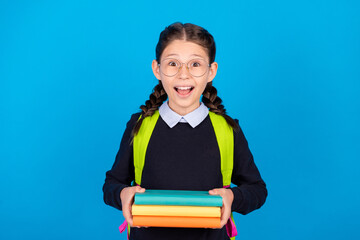 Photo of cheerful excited crazy schoolgirl in spectacles hold pile books prepare homework isolated on blue color background