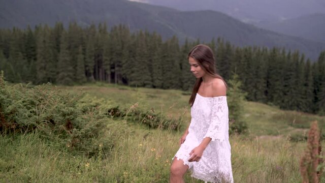 one young beautiful Caucasian woman in a white summer dress with bare feet is walking along the mountain slope against the background of mountain peaks. Copy space.
