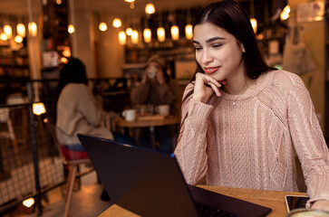 Portrait of young woman working on using laptop at coffee shop.