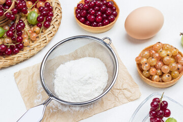 Flour in sieve, egg. Tartlets with berries.