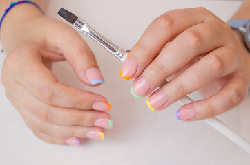 Women's hands with a brush on a white canvas background for drawing. French manicure with a multi-colored coating.