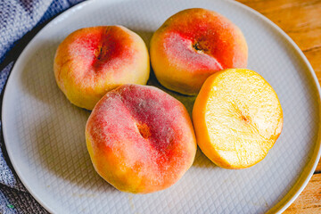 Naklejka na ściany i meble Fresh flat peach fruits on plate, cut close-up