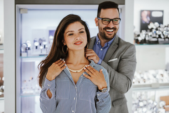 Middle Age Couple Enjoying In Shopping At Modern Jewelry Store. Young Woman Try It Out Gorgeous Necklace And Earrings.