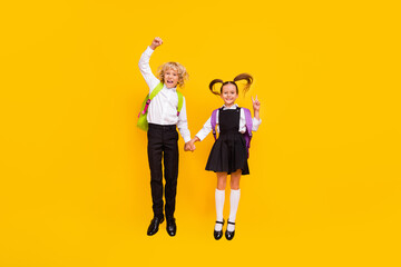 Photo of crazy children jump hold hands show victory sign wear school uniform isolated yellow color background