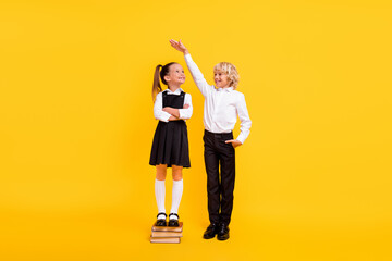 Photo of confident kids girl stay pile book boy measure height wear school uniform isolated yellow color background