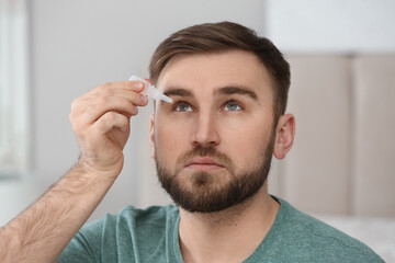 Obraz premium Young man using eye drops on blurred background