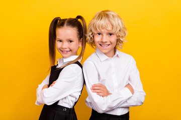 Photo of two self-assured schoolchildren crossed hands wear school uniform isolated yellow color...
