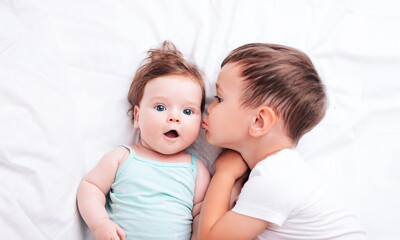 Fototapeta na wymiar a little beautiful brother kisses his newborn sister on the cheek while lying on the bed