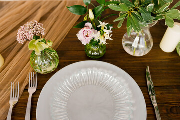 Serving a festive table. Beautiful plates and cutlery, flowers in vases on a wooden table. Top view