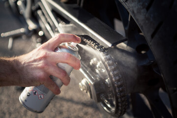 Man's hand using spray can to clean and protect motorbike chain. Concept of maintenance and...