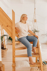 Young woman posing, having fun while sitting on a wooden staircase in a scandinavian style house