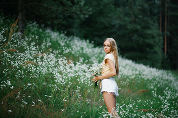 Naklejka na ściany i meble A girl in a field with flowers. Beautiful young woman in a field with white meadow flowers.
