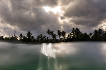 moody clouds with sun rays and palm trees at the beach