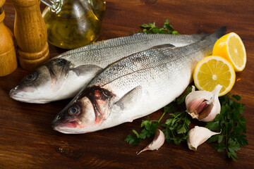 Raw European basses with lemon, parsley, garlic and spices on wooden background..