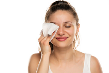 A smiling woman cleans makeup from her face with wet wipe - obrazy, fototapety, plakaty