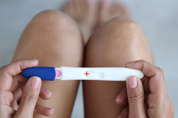 Seated woman holding positive pregnancy test closeup