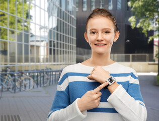 technology, health and people concept - happy smiling teenage girl in pullover showing smart watch with qr code on screen over grey background