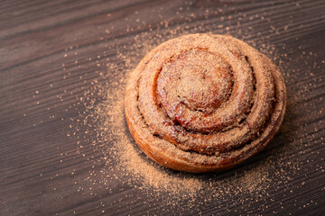Fototapeta na wymiar One tasty bun heavily flavoured with cinnamon on dark wooden table. Cooking spicy bread at home