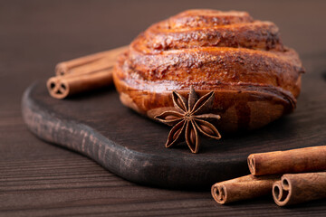 Beautiful composition of cinnamon bread on dark wooden table with sticks of cinnamon around and an anise star. Baking at home