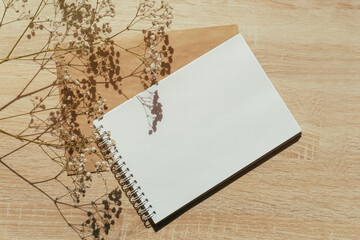 Notebook with clean beige sheets on wooden table next to sprig of gypsophila flowers. Concept of ready-made mockup for recording, time planning, notes. Close-up, copy space, beige pastel background
