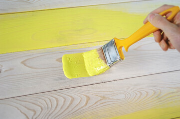 Closeup female hand with paintbrush painting a natural wooden door with yellow paint. The concept of colored bright creative interior design for a young family. How to paint a wooden surface