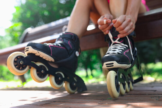 Young woman puts on roller skates in park closeup