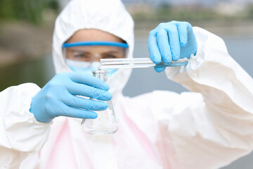Scientist in protective suit and goggles in takes of water samples in test tube from lake closeup