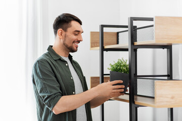 home improvement, decoration and people concept - happy smiling man placing flower in pot or houseplant to shelf