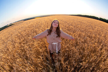 Happy woman stands in a wheat field in the summer against the background of a setting sun