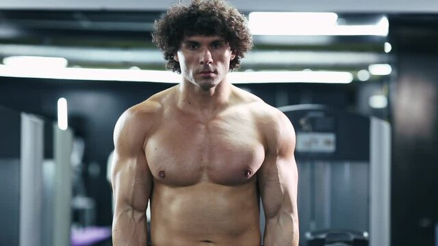 curly hair brutal sexy strong bodybuilder athletic fitness manpumping biceps muscles with parallel bar face to the camera workout bodybuilding concept background