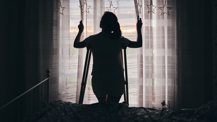 Silhouette of a woman on crutches by the window. Rehabilitation after physical trauma.