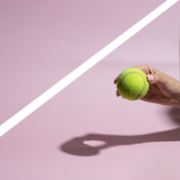 Hand holding  tennis ball on pink background with whte line.