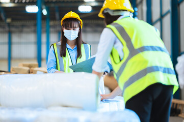 Team engineers and foreman or technicians males and females wear a mask, hard hat and vest. Standing, consult discuss industrial production management through data files within the factory.